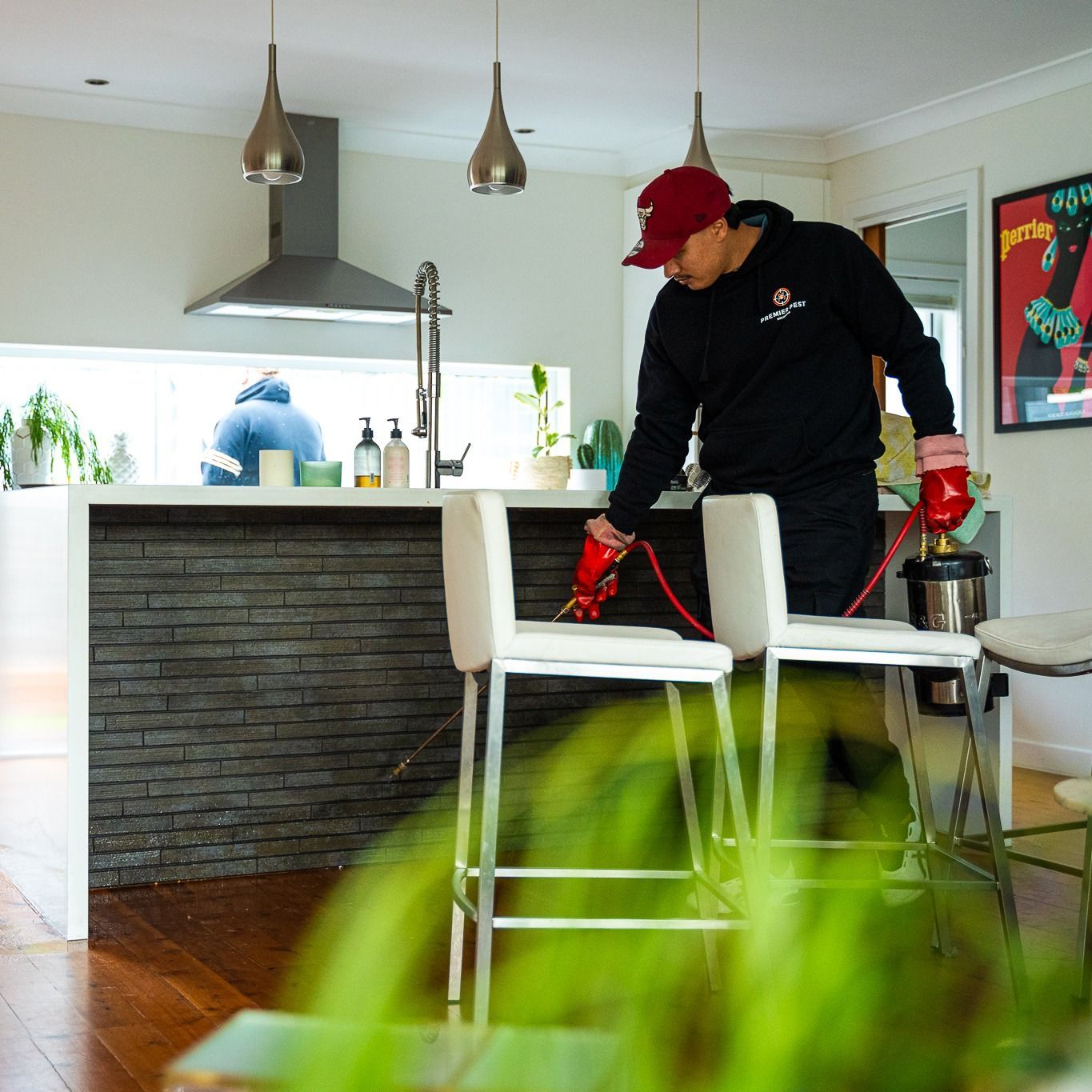 Man in Black Outfit and Red Hat Sprays in a Kitchen — Premier Pest Control Wollongong In Parramatta, NSW