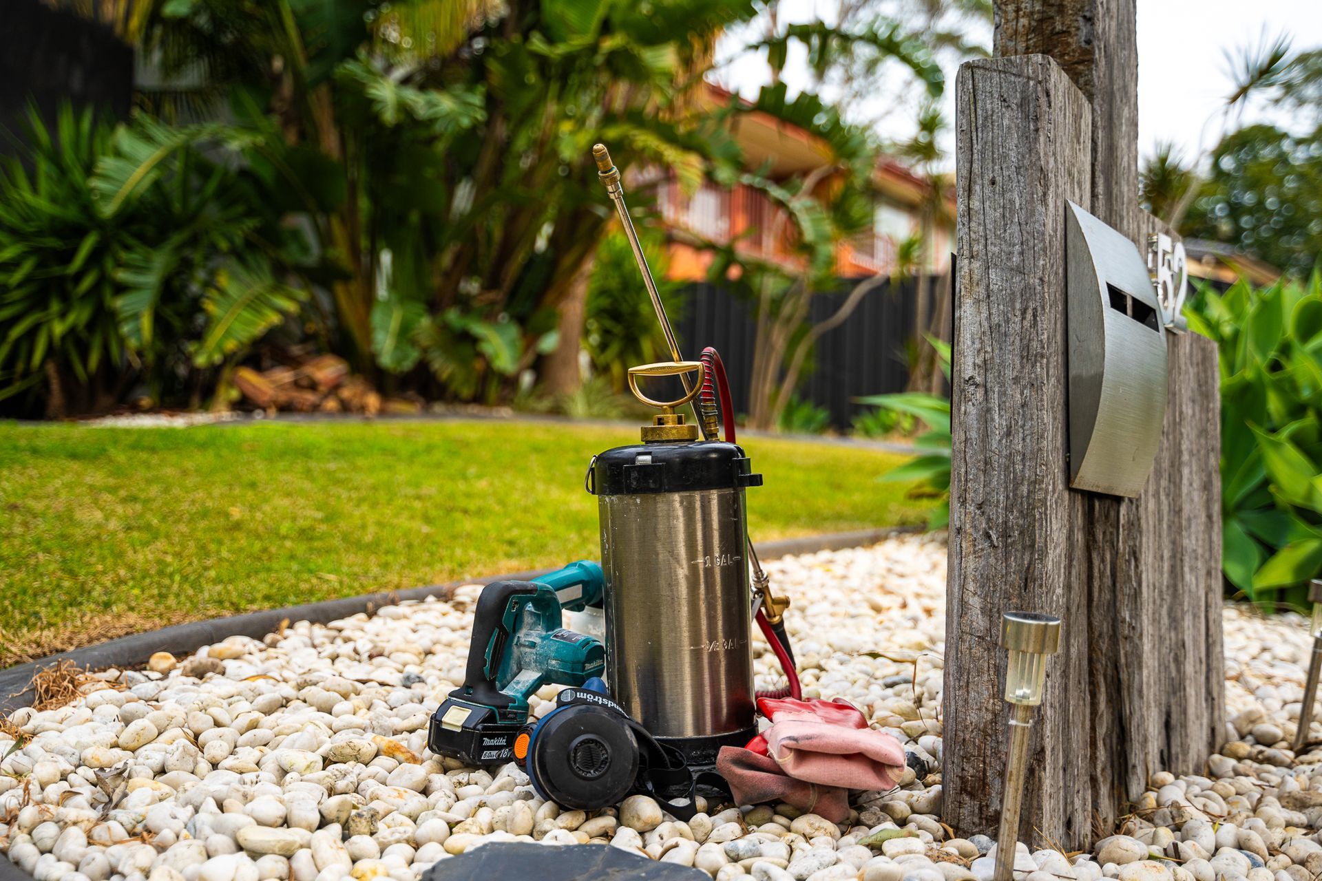 Stainless steel pest control sprayer on a bed of white pebbles next to a wooden post and mailbox. — Premier Pest Control Wollongong In Campbelltown, NSW