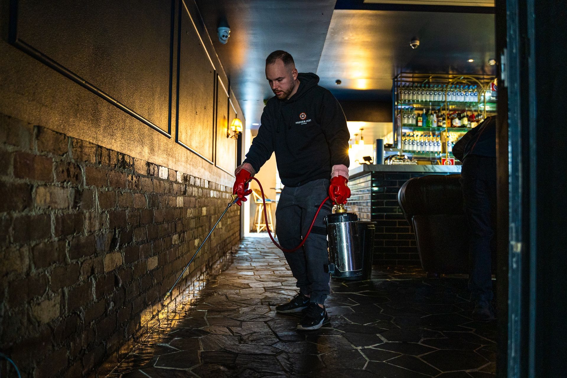 A Man Is Spraying A Brick Wall With A Sprayer — Premier Pest Control Wollongong In Shellharbour, NSW