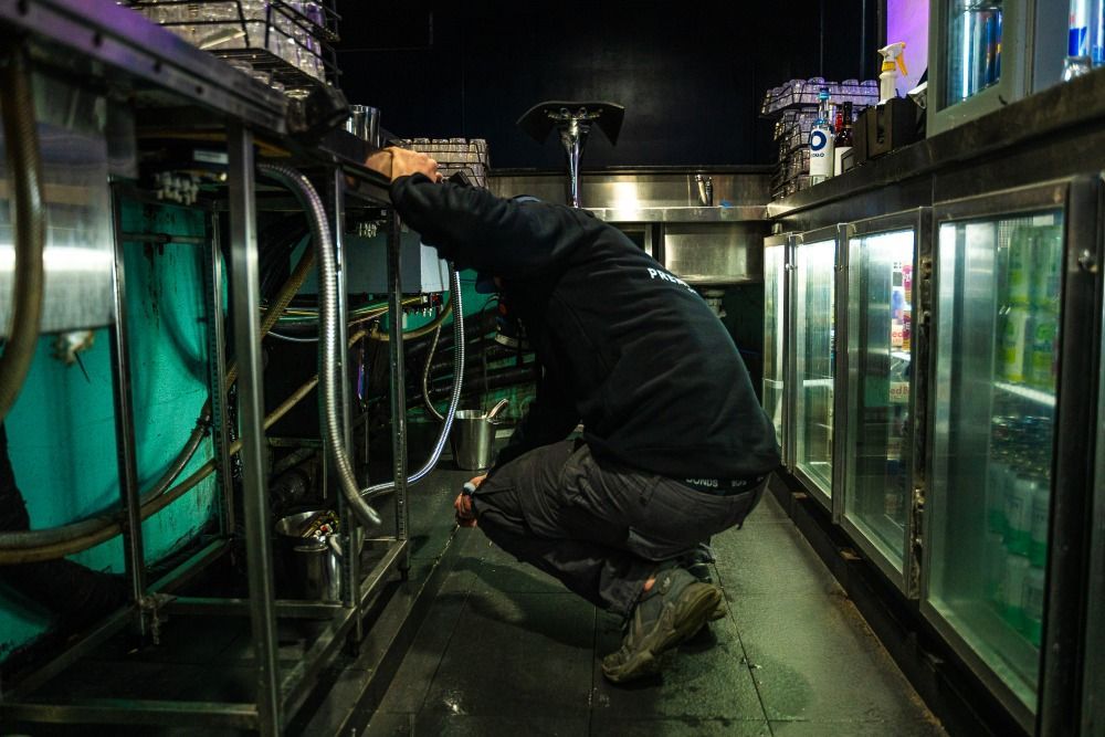 A Man Is Kneeling Down In A Kitchen Working On A Machine — Premier Pest Control Wollongong In Wollongong, NSW
