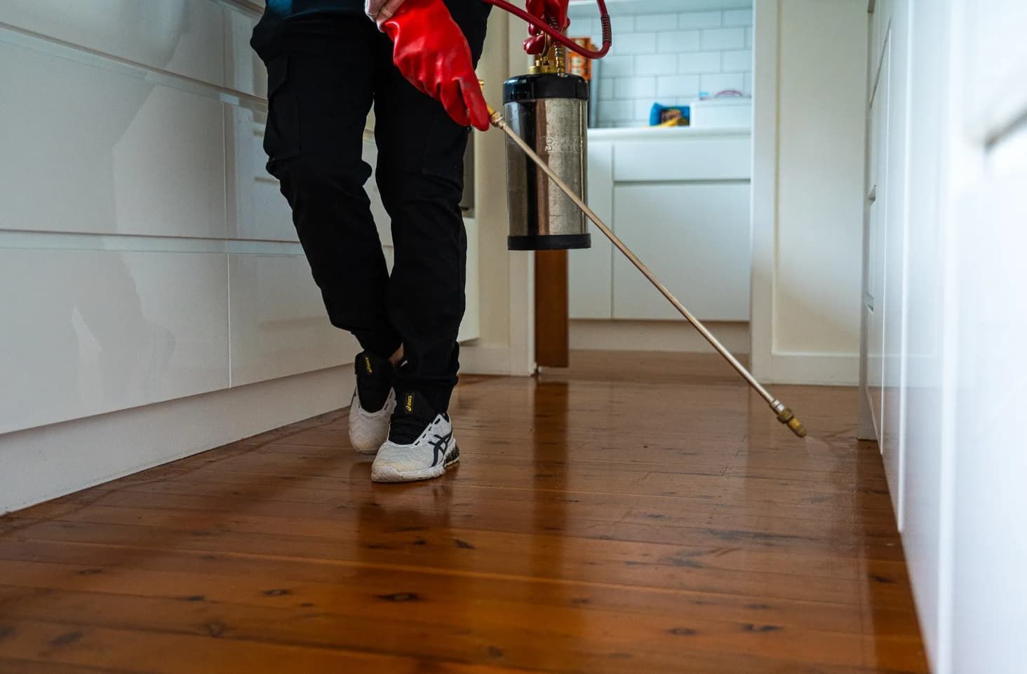 A Person Is Spraying A Wooden Floor With A Sprayer — Premier Pest Control Wollongong In Wollongong, NSW