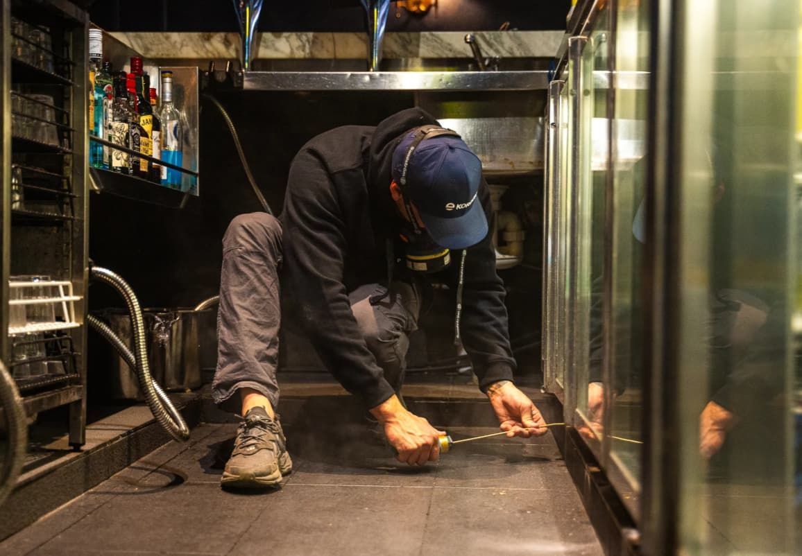 A Man Is Measuring The Floor Of A Kitchen With A Tape Measure — Premier Pest Control Wollongong In Wollongong, NSW
