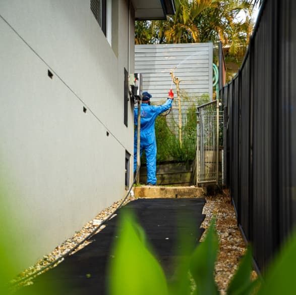 A Man In A Blue Suit Is Spraying A Wall With A Hose — Premier Pest Control Wollongong In Wollongong, NSW