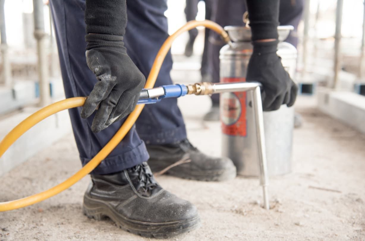 Person in Work Clothes Holding a Hose Connected to a Silver Tank — Premier Pest Control Wollongong In Sutherland Shire, NSW