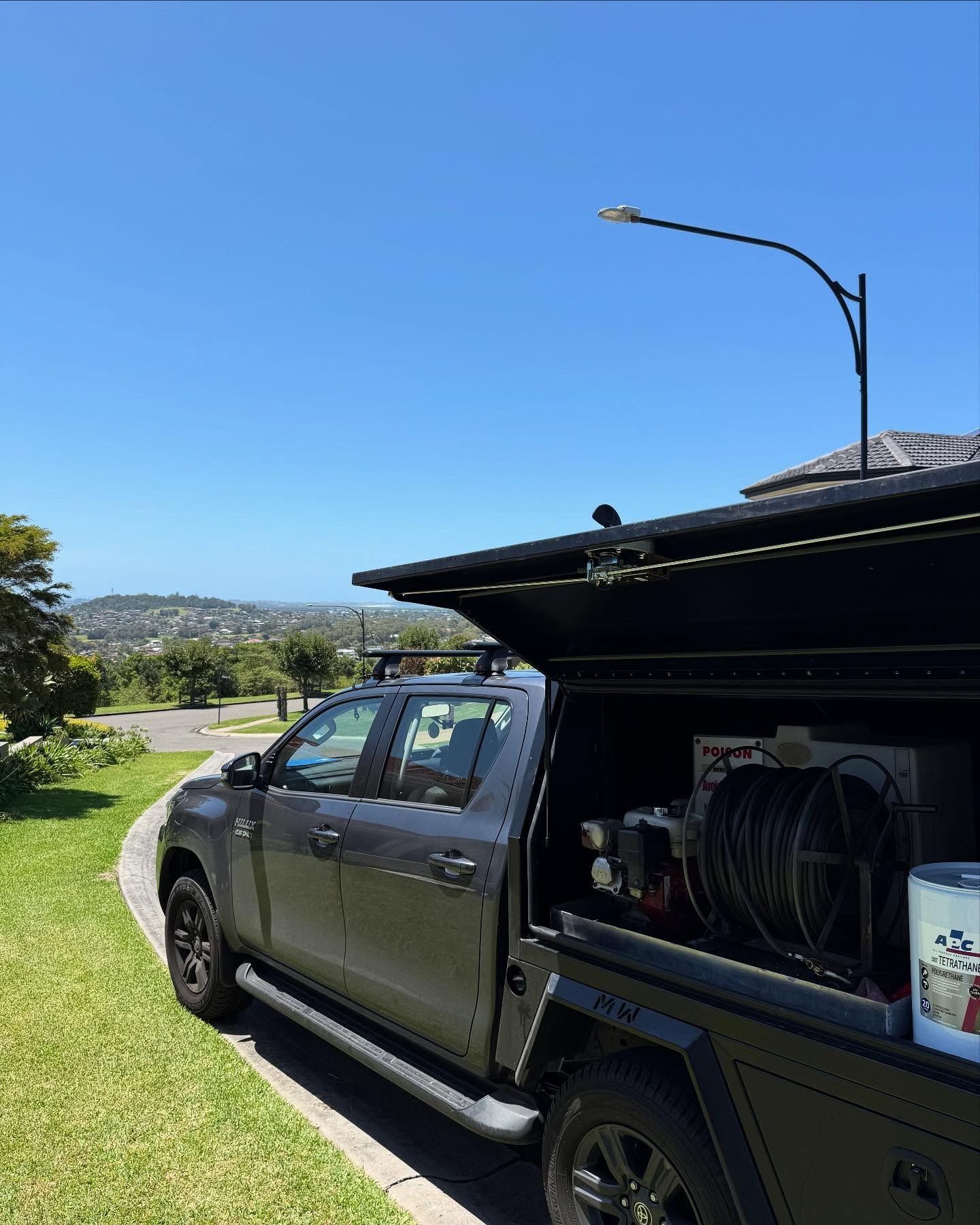 Dark gray truck parked on a driveway with an open bed, equipment inside, street light overhead. Green grass, blue sky