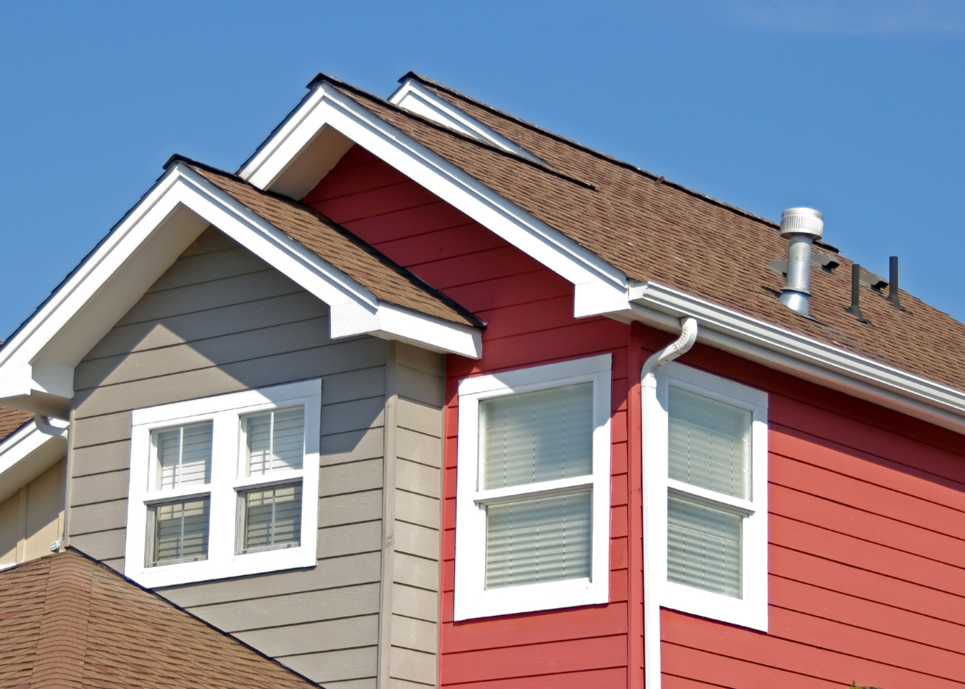 Two-story house with brown roof and red and gray siding against a blue sky.