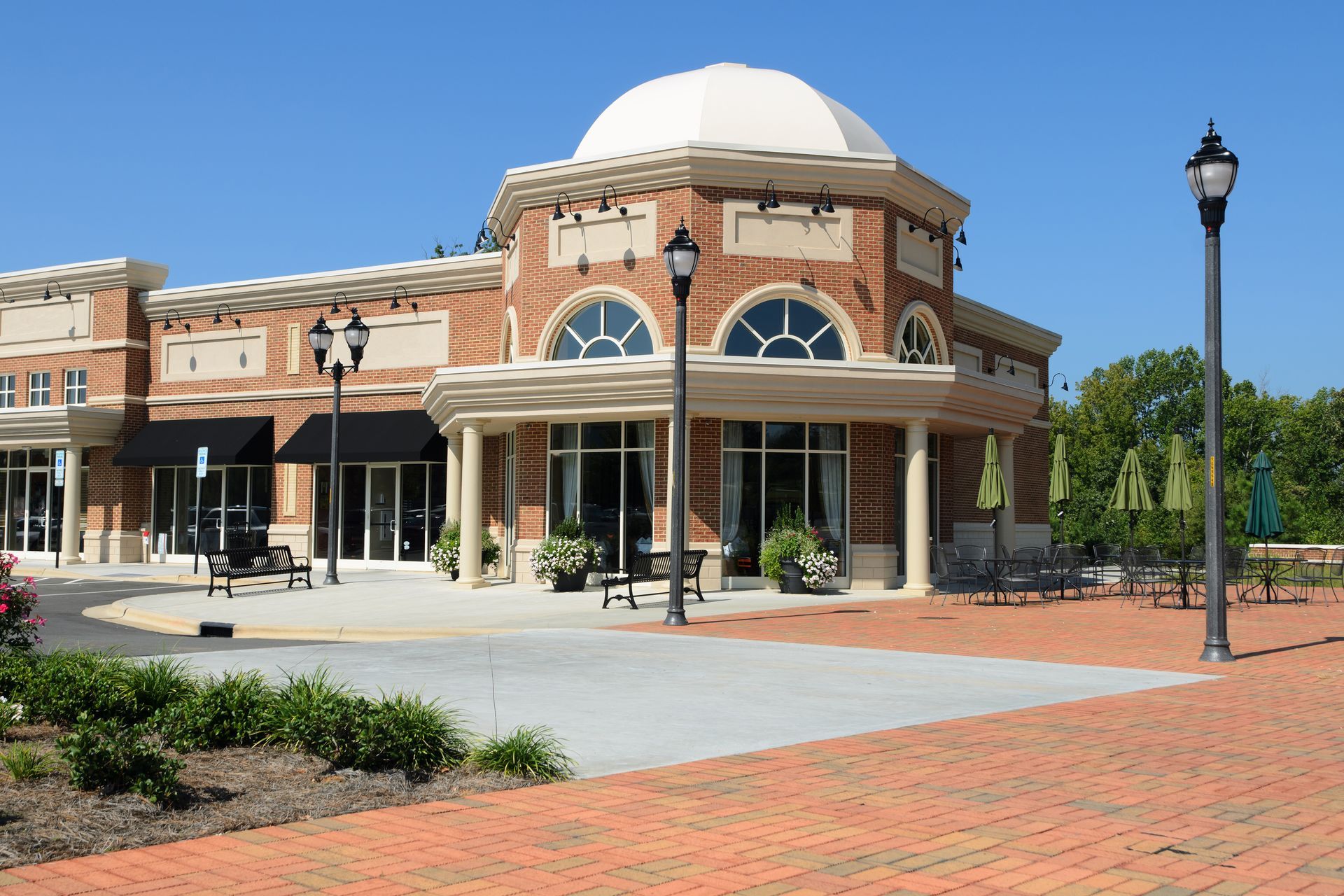 Brick commercial building with a white dome, outdoor seating, and streetlights on a sunny day.