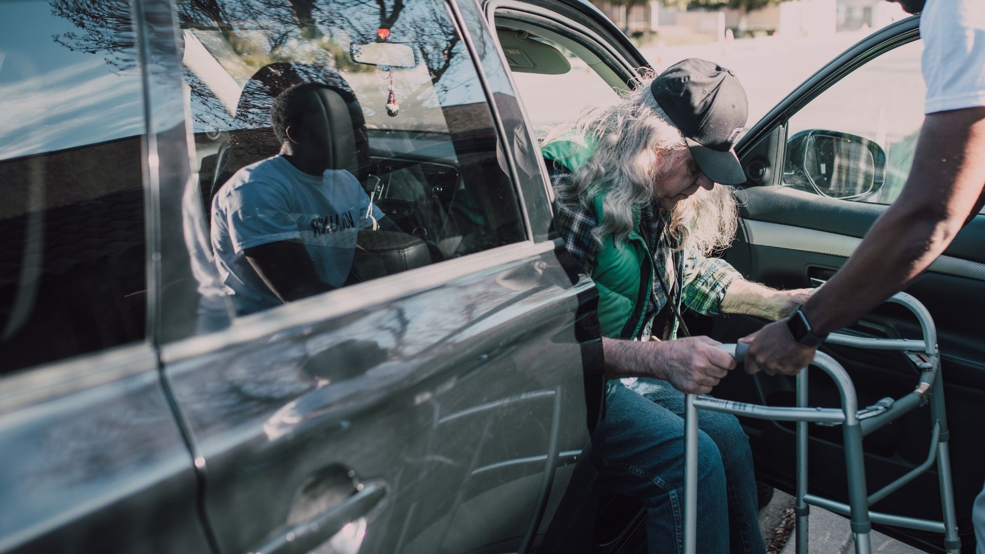 A man is helping an elderly woman with a walker into a car.