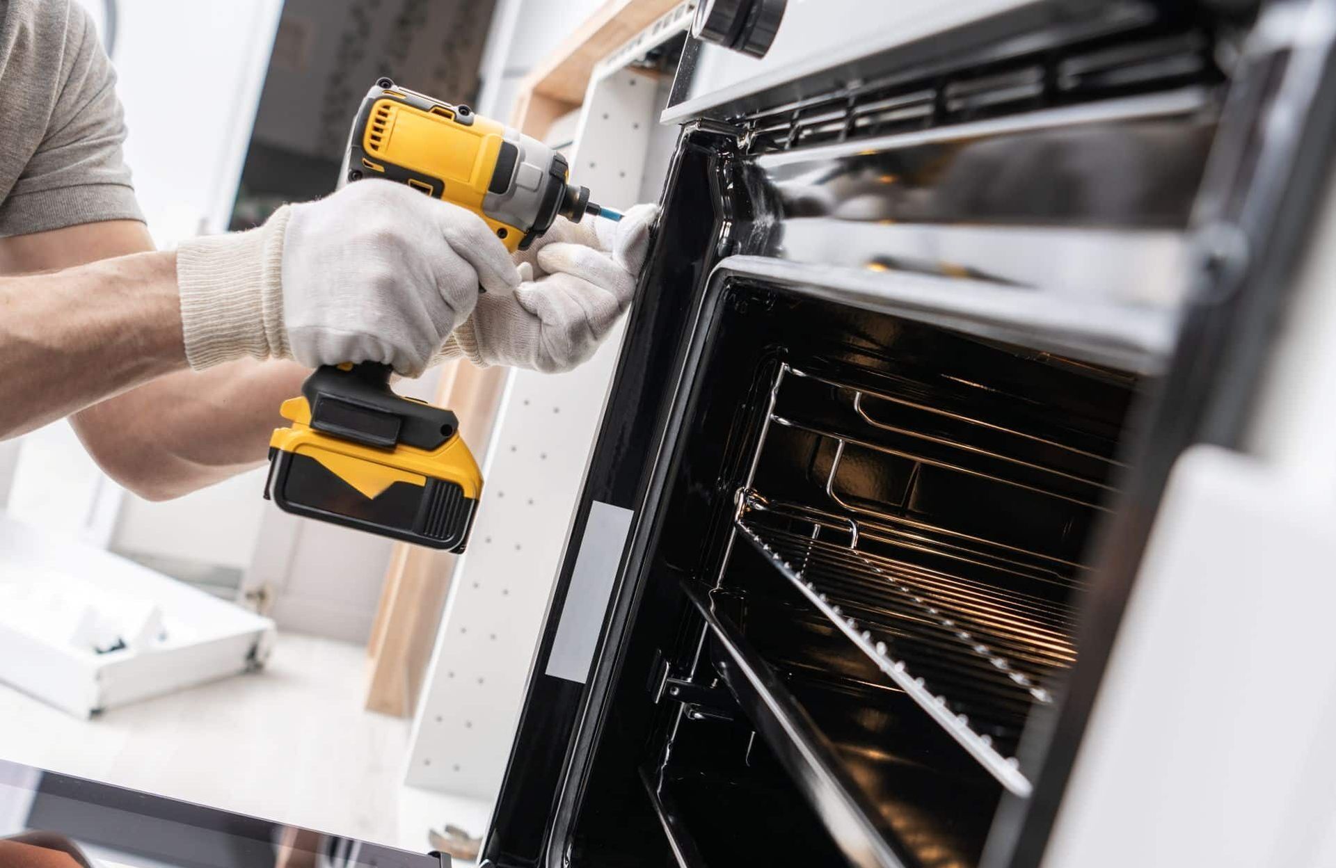 Person in gloves using a yellow drill to repair an oven.