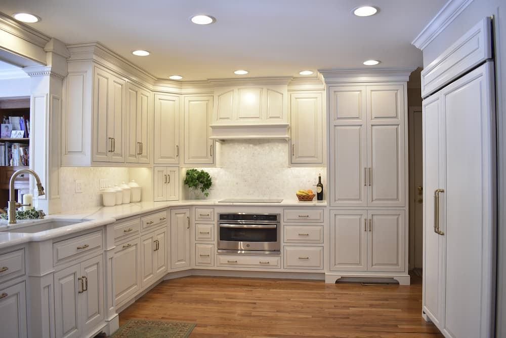 White kitchen with cabinets, appliances, marble countertops, and hardwood floors.