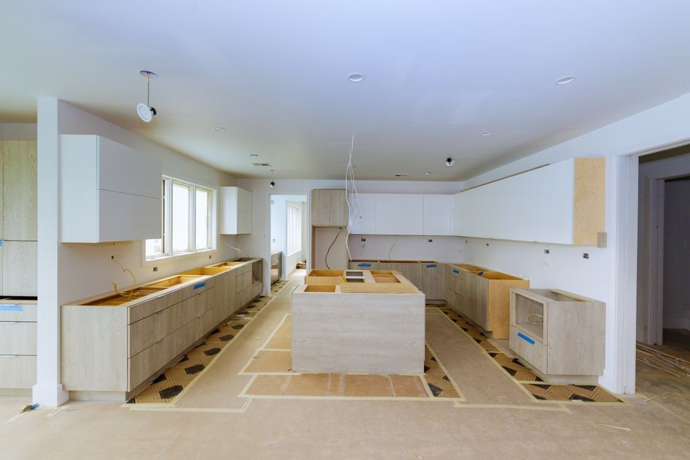 Kitchen under construction with light wood cabinets and island; walls are white.