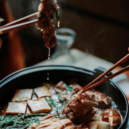 A person is holding chopsticks over a pot of food.