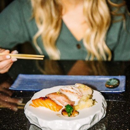 A woman is eating sushi with chopsticks at a restaurant