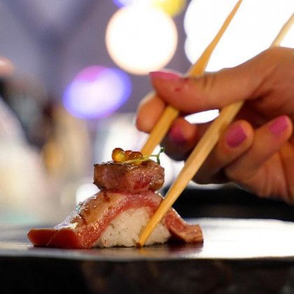 A person is holding chopsticks over a piece of sushi