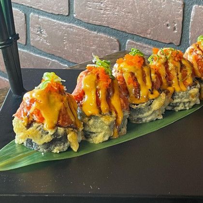 A row of sushi rolls on a green leaf on a black plate.