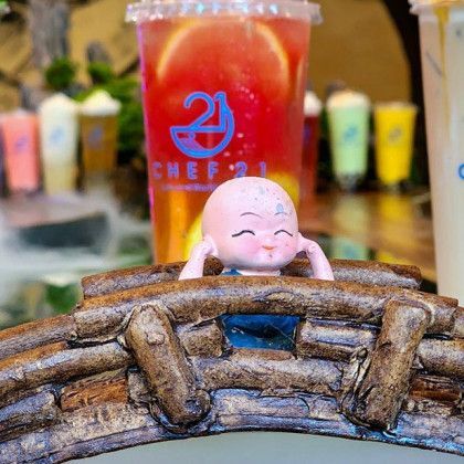 A doll is sitting on a wooden bridge next to a cup of tea.