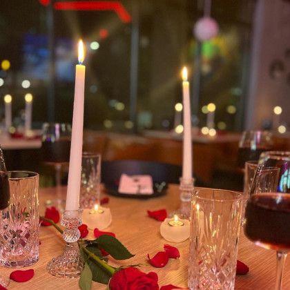 A table with candles , wine glasses , roses and petals on it.