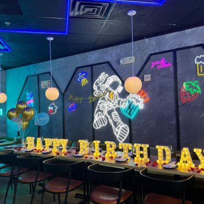 A room with tables and chairs and a neon sign that says `` happy birthday ''.