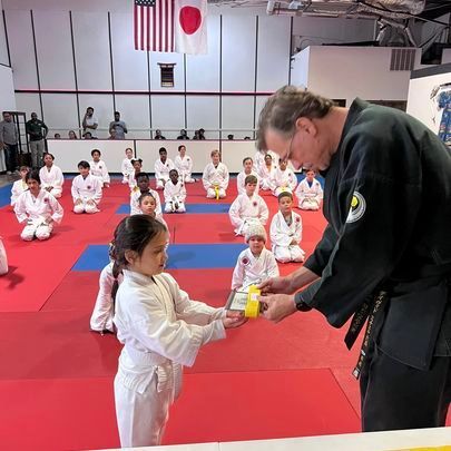 A man is giving a certificate to a young girl in a karate class.