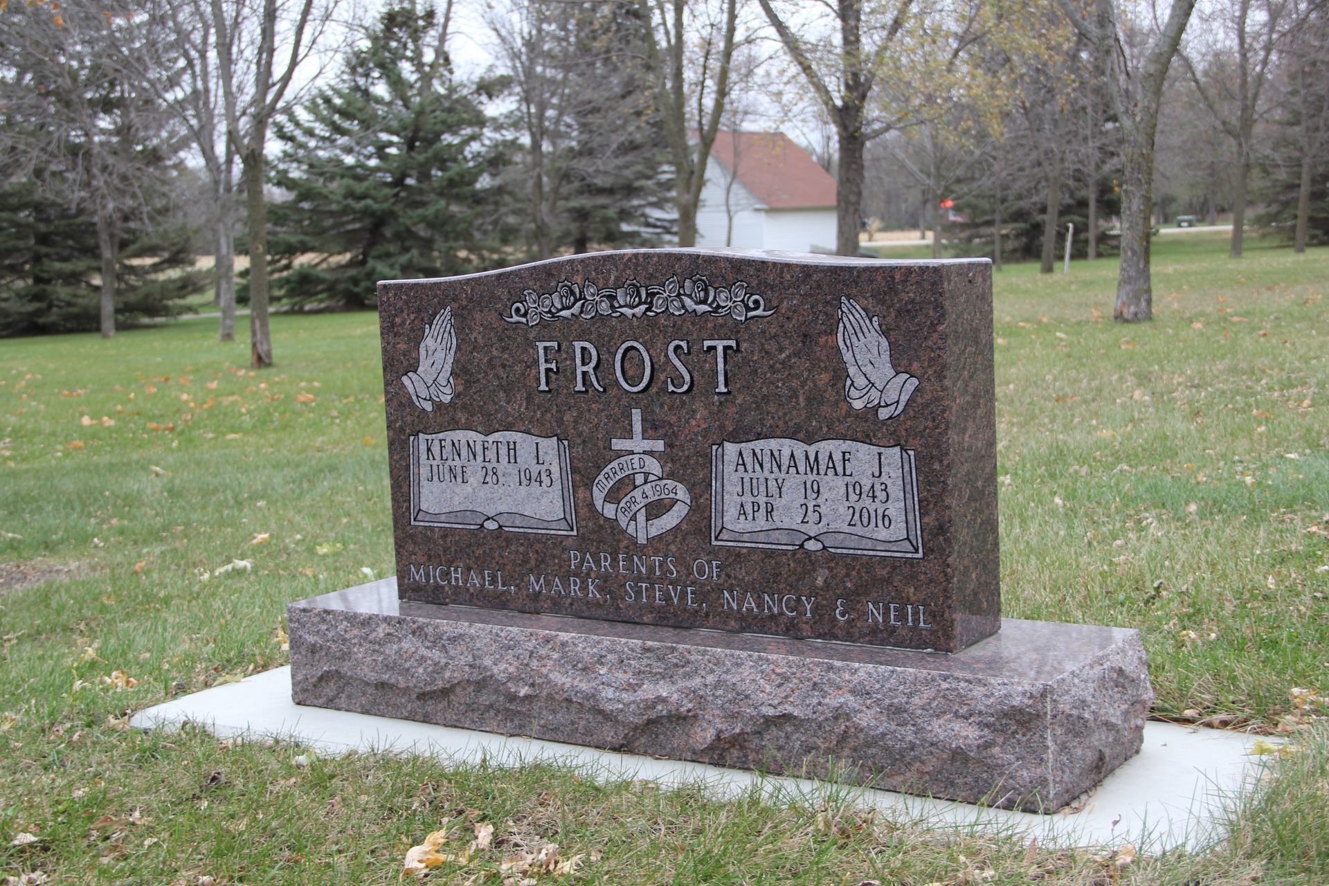 Grave marker for the Frost family. Brown granite with carved text, heart, and praying hands; set in a grassy cemetery.