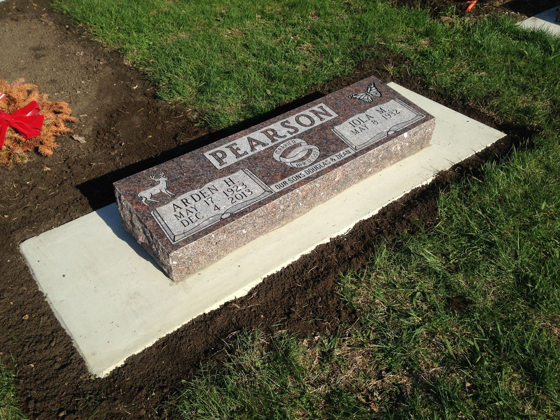 A rectangular granite headstone on a concrete base in a cemetery plot.