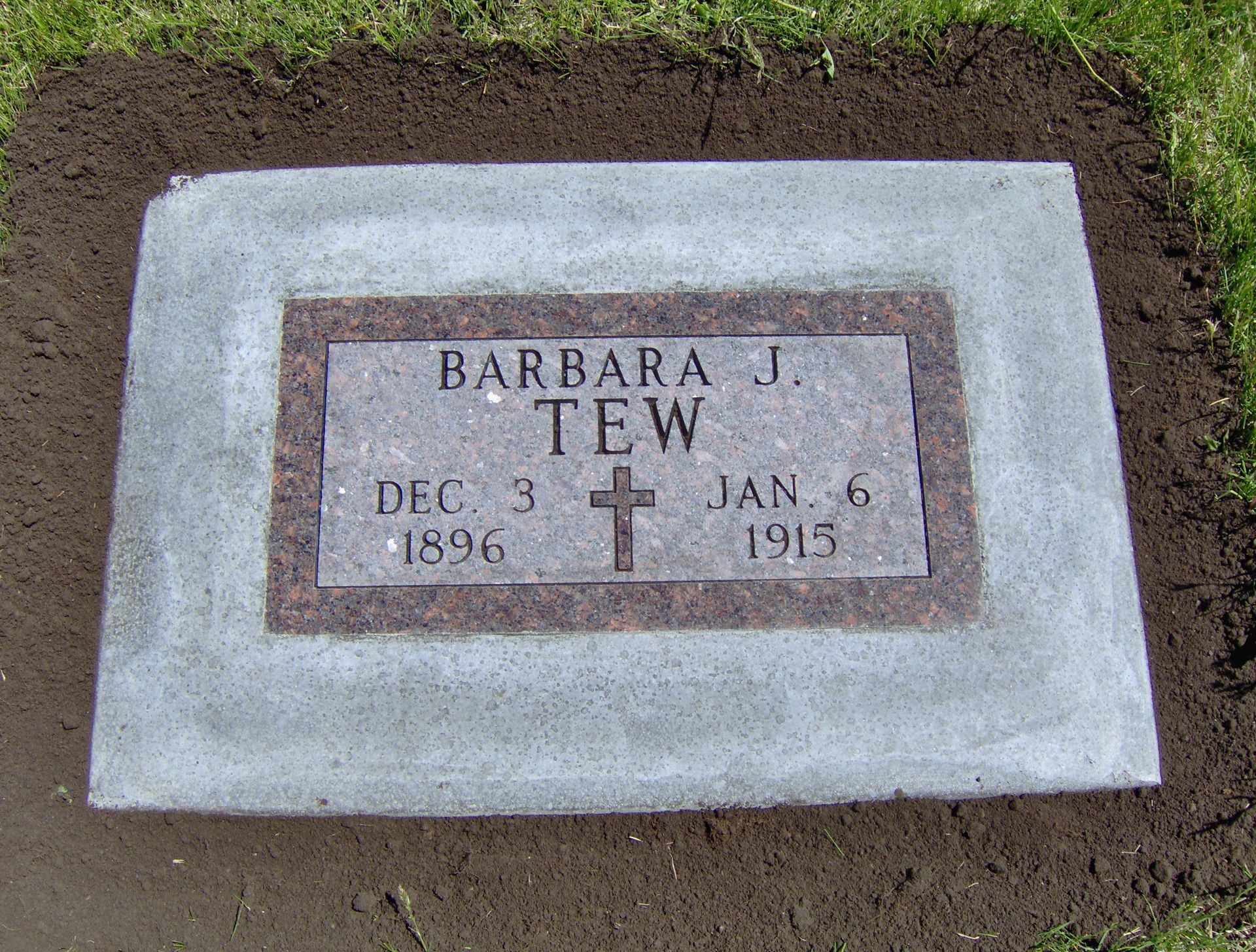 Headstone for Barbara J. Tew, with birth/death dates of Dec 3, 1896 - Jan 6, 1915. Gray stone with brown trim, outdoors.