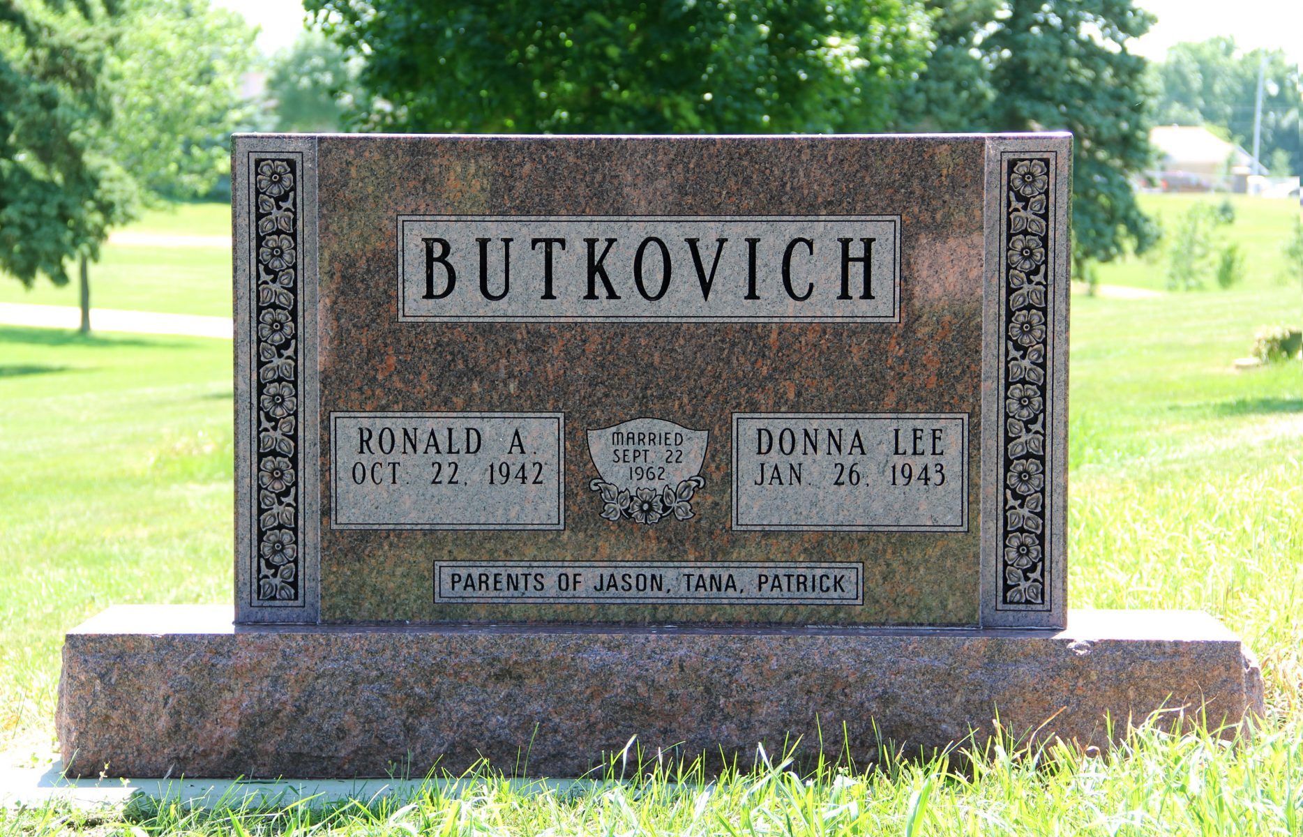 Gravestone for Butkovich family with names and dates, set in a grassy cemetery.