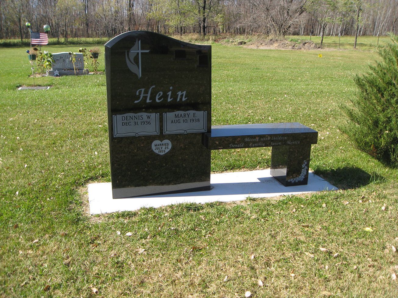 Black headstone with built-in bench in a grassy cemetery. The headstone has the name