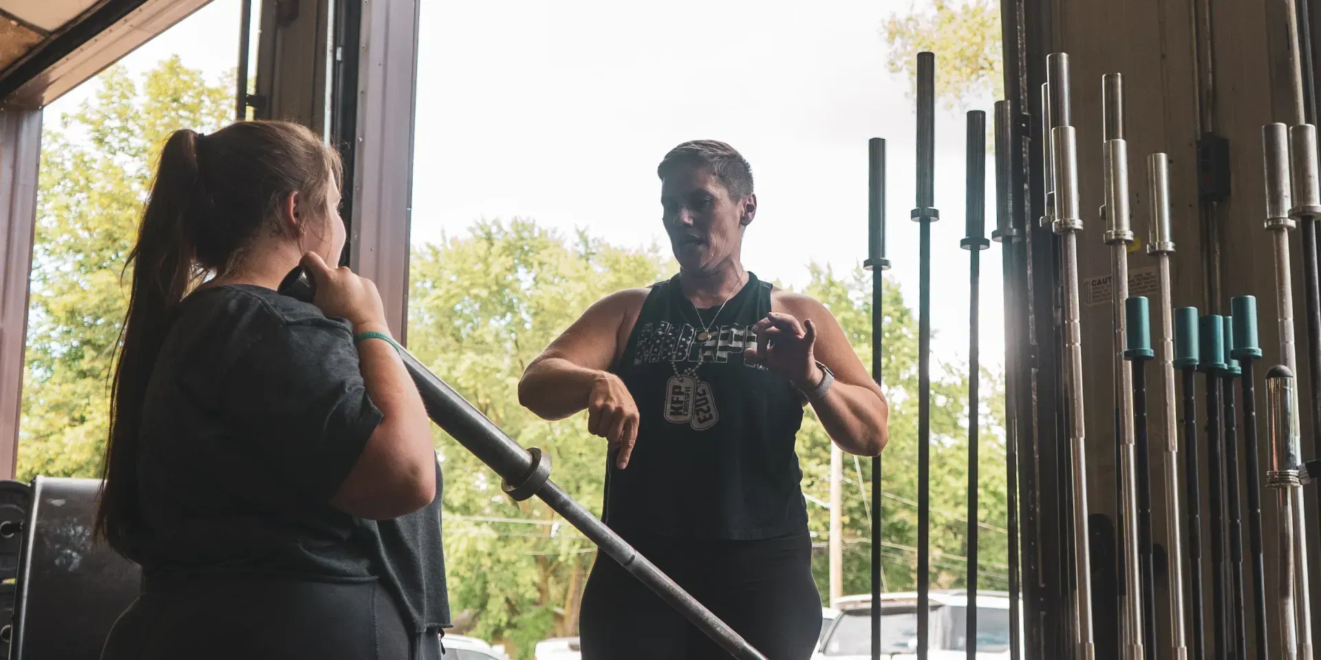 A man is talking to a woman in a gym while holding a barbell in a New Port, MN fitness class