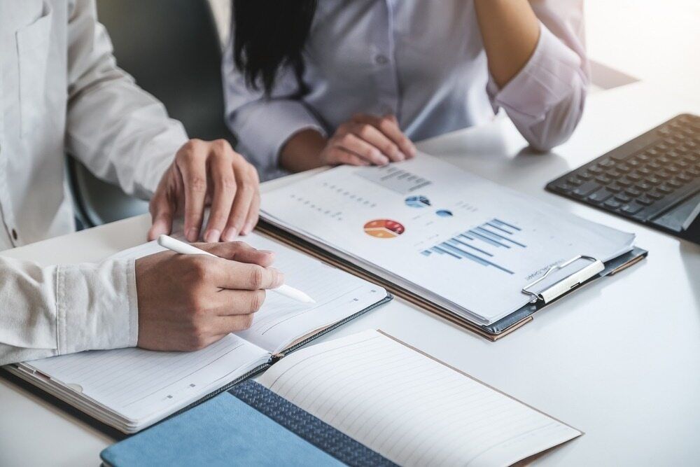 A Man And A Woman Are Sitting At A Table Looking At A Clipboard Adelaide — Tradie Books Australia In Adelaide, SA