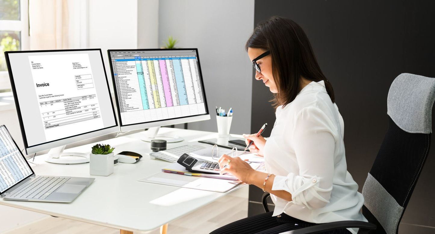 A Woman Is Sitting At A Desk With Two Computer Monitors And A Laptop — Tradie Books Australia In Port Kennedy, WA