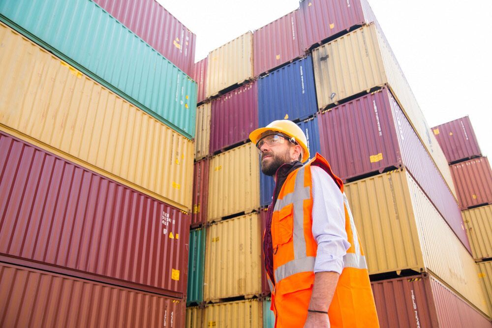 A Man In An Orange Vest And Hard Hat Is Standing In Front Of Shipping Containers — Tradie Books Australia In Port Kennedy, WA