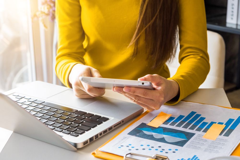 A Woman Is Sitting At A Desk With A Laptop And A Tablet — Tradie Books Australia In Port Kennedy, WA