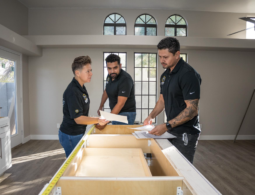 A group of people are working on a kitchen in an empty room.