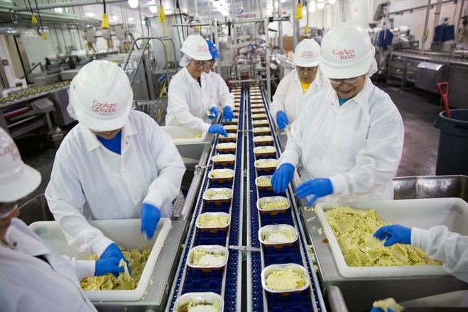 A group of people are working in a kitchen preparing food on a conveyor belt.