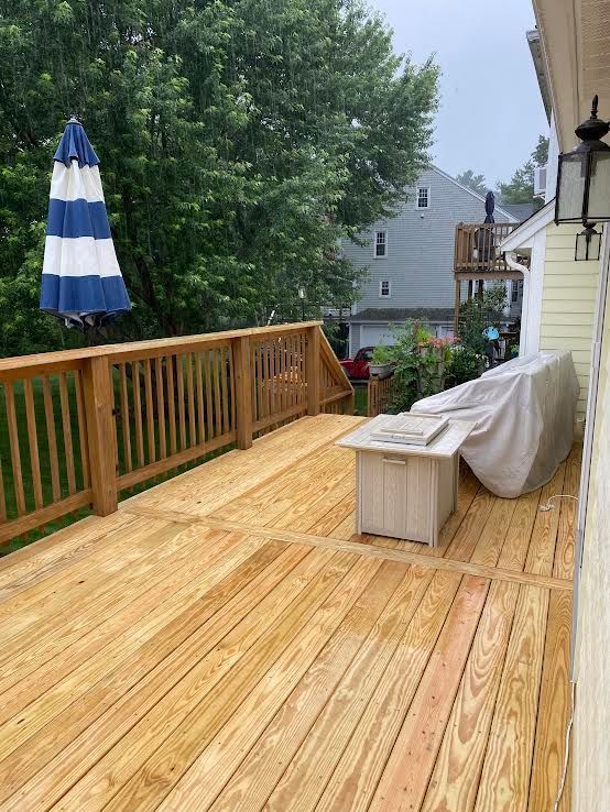A freshly stained wooden deck with a wooden railing, a blue and white striped umbrella, and a covered grill set.