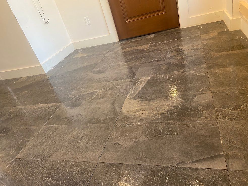 A glossy, gray stone tile floor leads toward a closed wooden door in a room with white walls and trim.