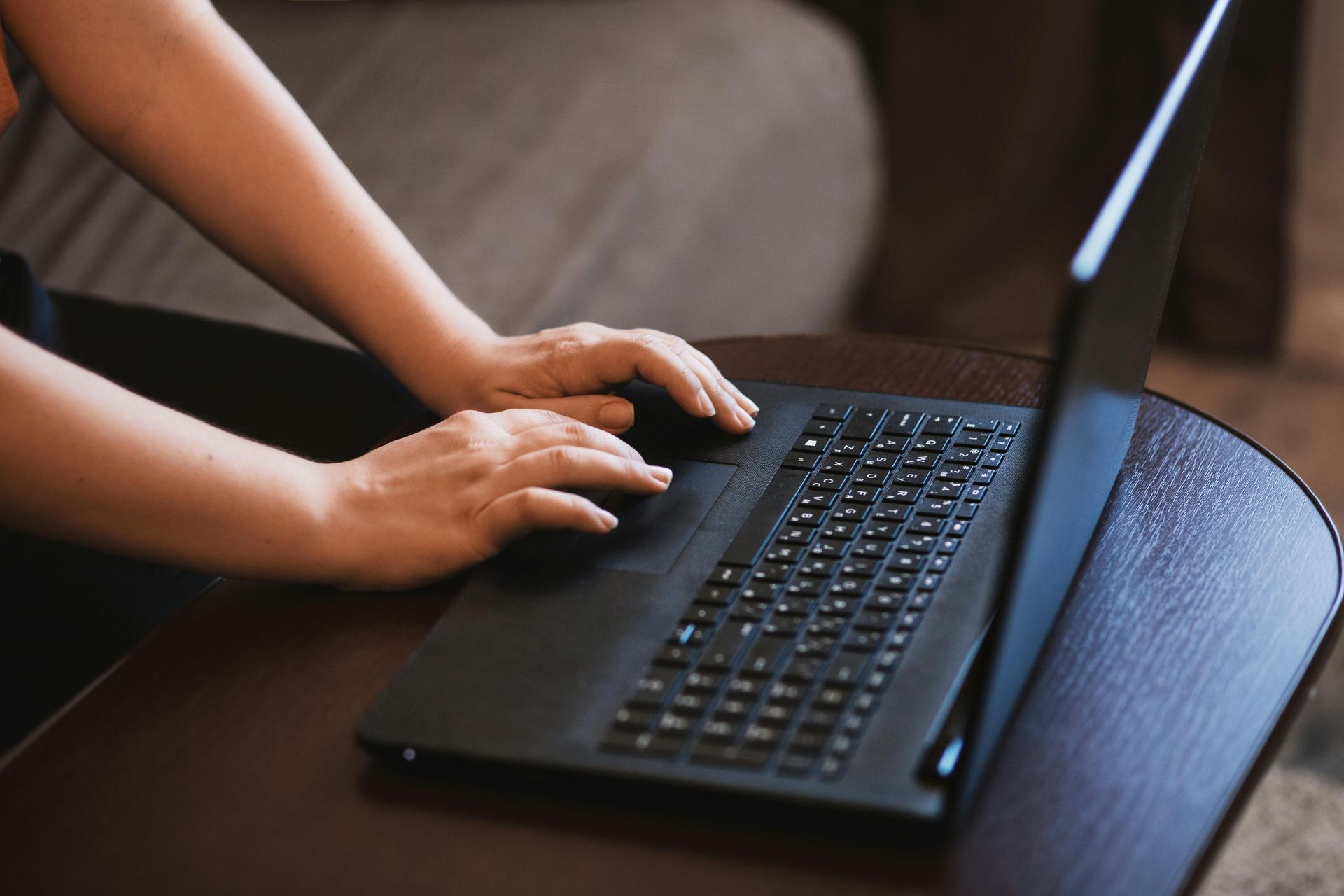 Hands typing on a black laptop keyboard resting on a wooden desk.