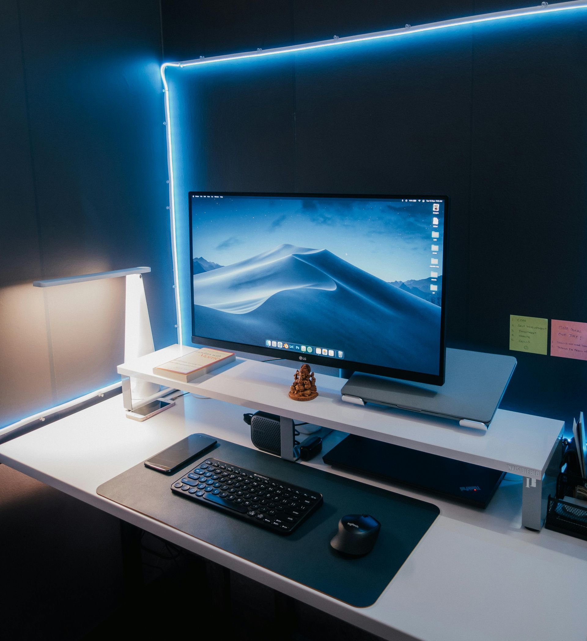 A modern desk setup with a computer monitor, keyboard, and mouse on a white desk illuminated by blue LED strip lighting.