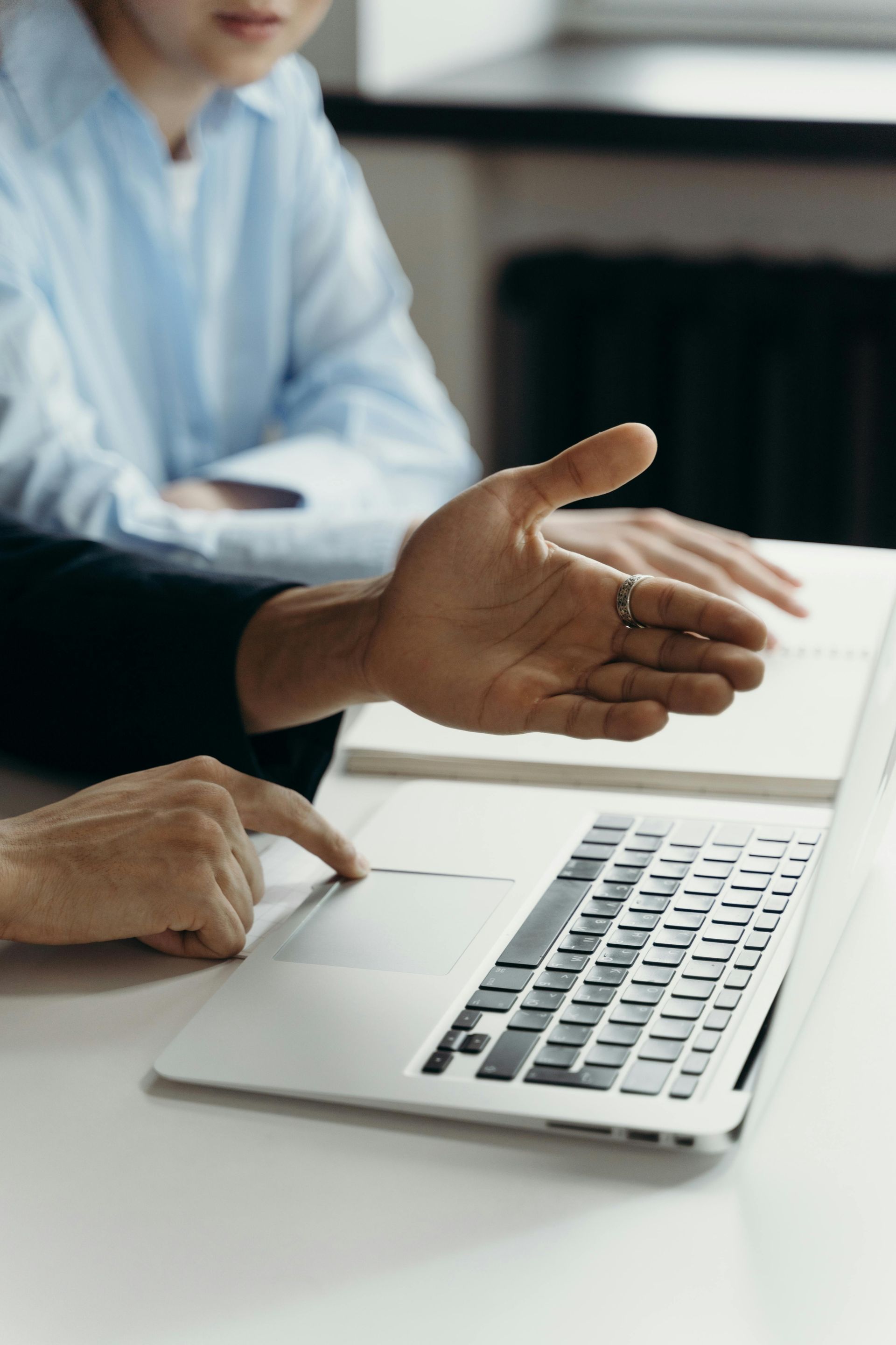 Two people collaborate at a desk, with one pointing at a laptop screen while the other gestures with an open hand.