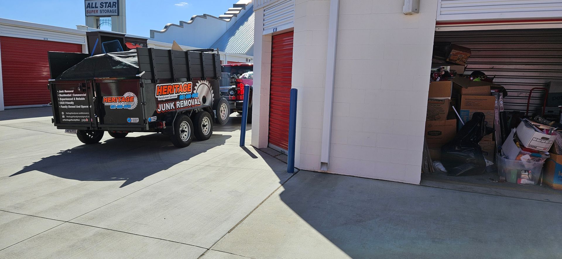 A truck with a trash container parked next to a storage unit, loaded with boxes and bags.