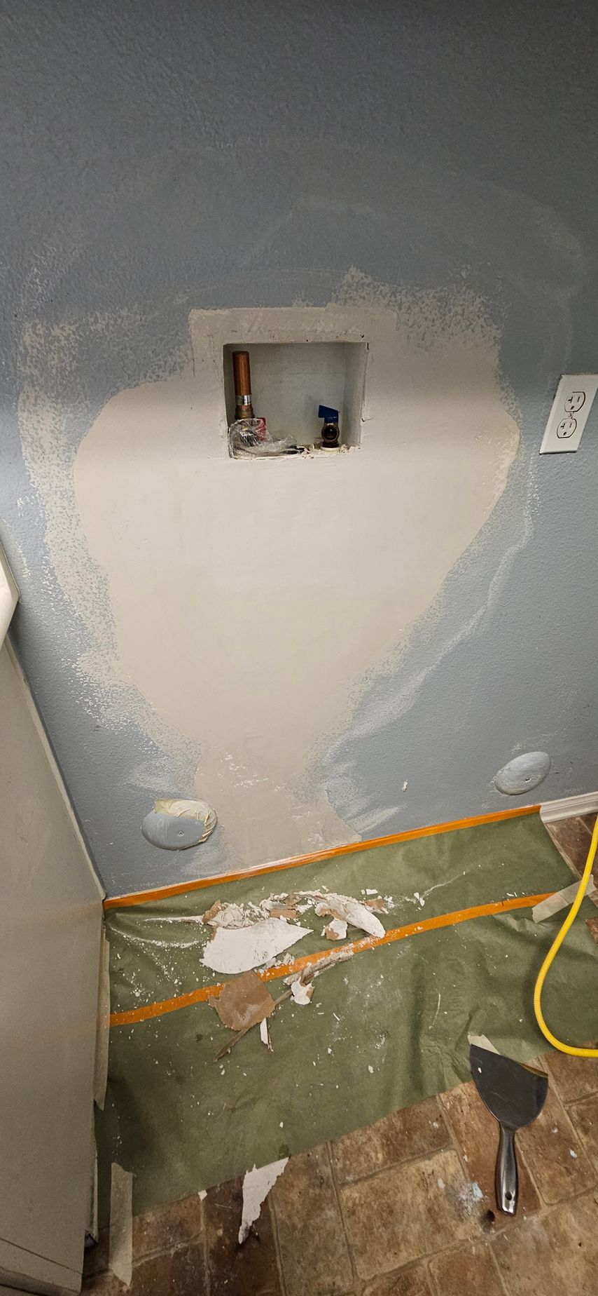 Wall repair with drywall and a recessed section, covered by a green tarp on the floor.