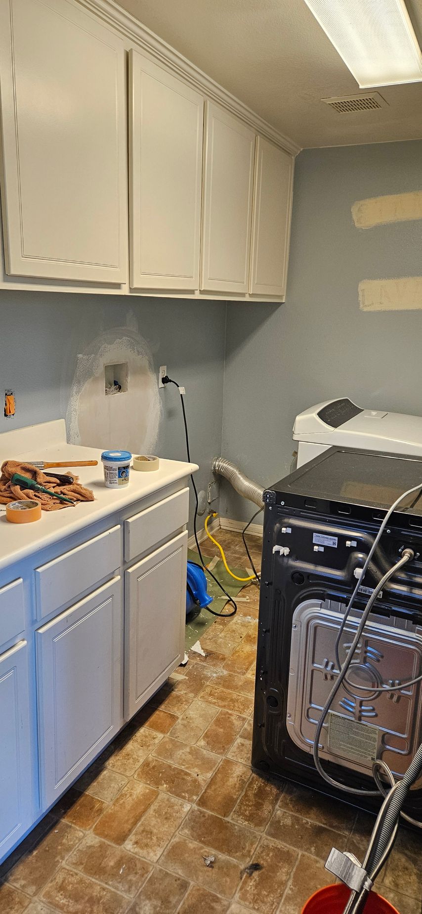 Laundry room with white cabinets, countertop, and appliances. Wires and debris on the floor.
