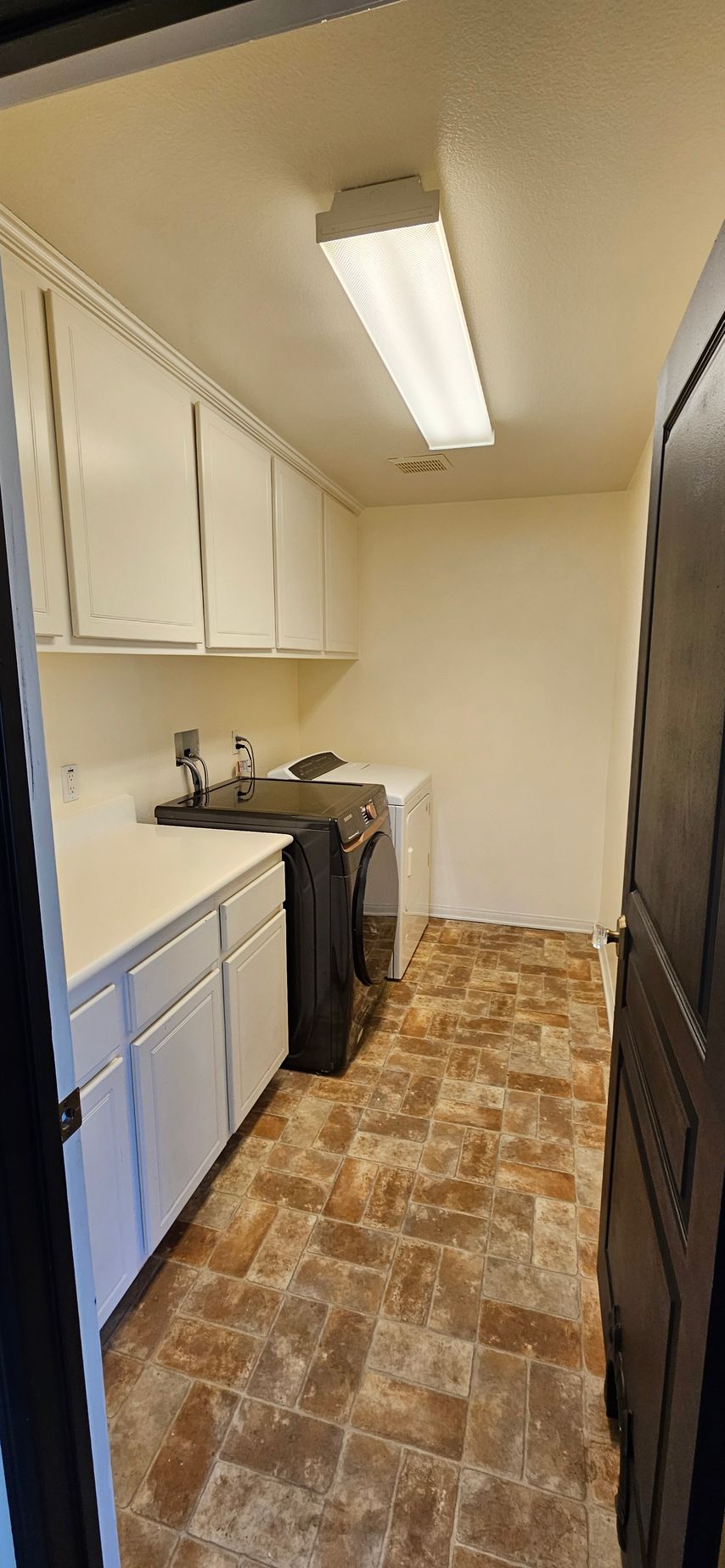 Laundry room with white cabinets, countertop, appliances, and brown tiled floor.