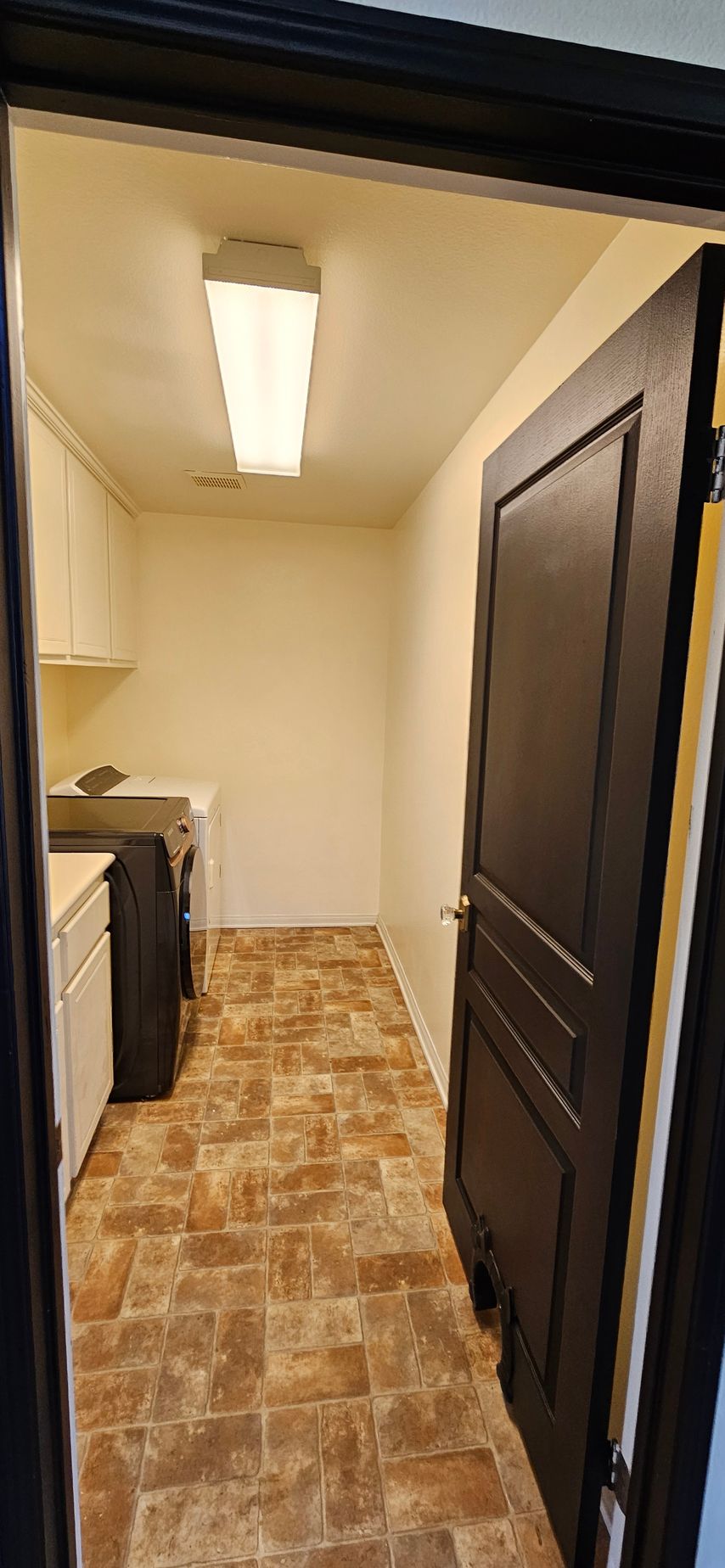 A laundry room with a washing machine, dryer, and cabinet. The door is open.