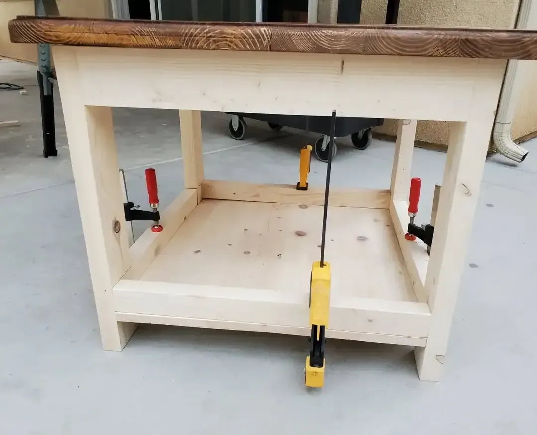 Wooden table under construction, held together by clamps. Light wood frame with a dark stained top.