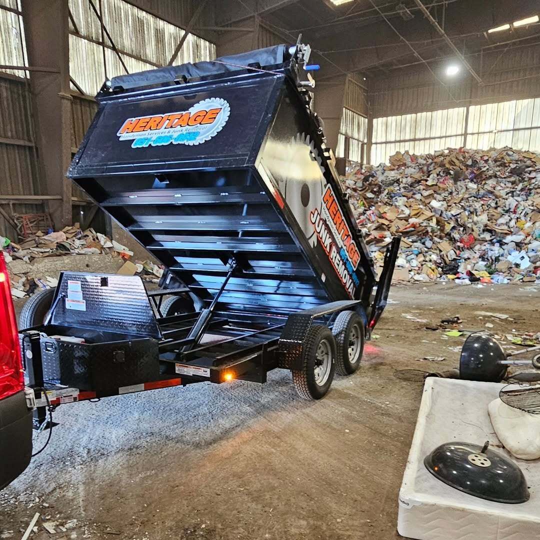 Black dump trailer unloading gravel inside a warehouse, a large pile of debris in the background.