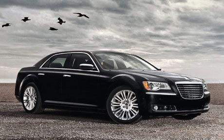 A black car is parked on a gravel road with birds flying in the background.