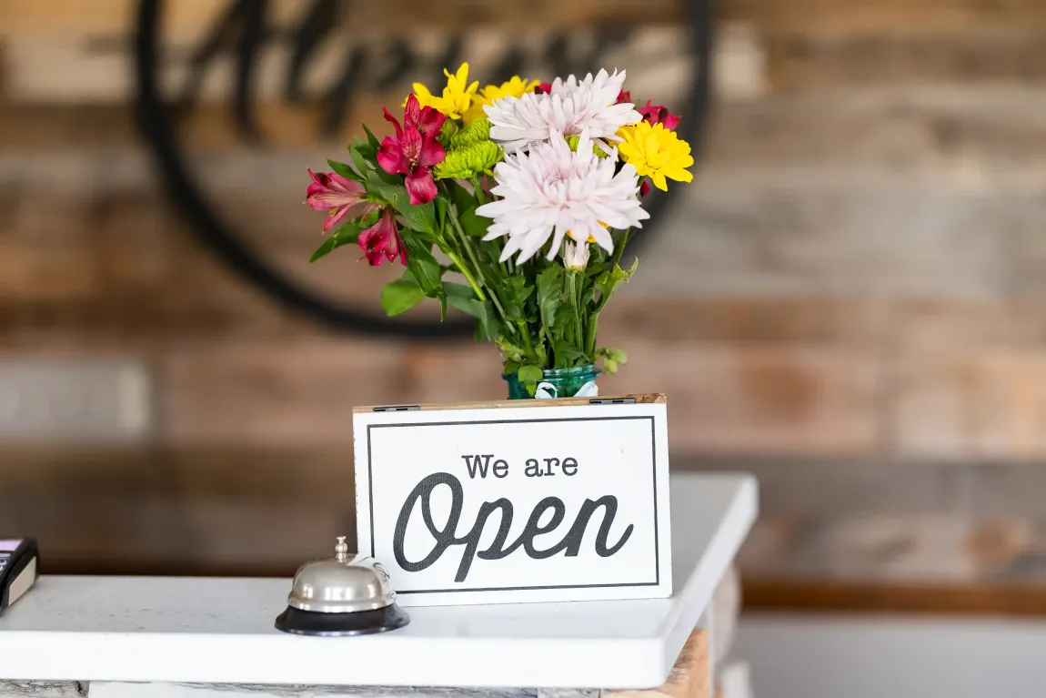 A sign that says `` we are open '' next to a vase of flowers.
