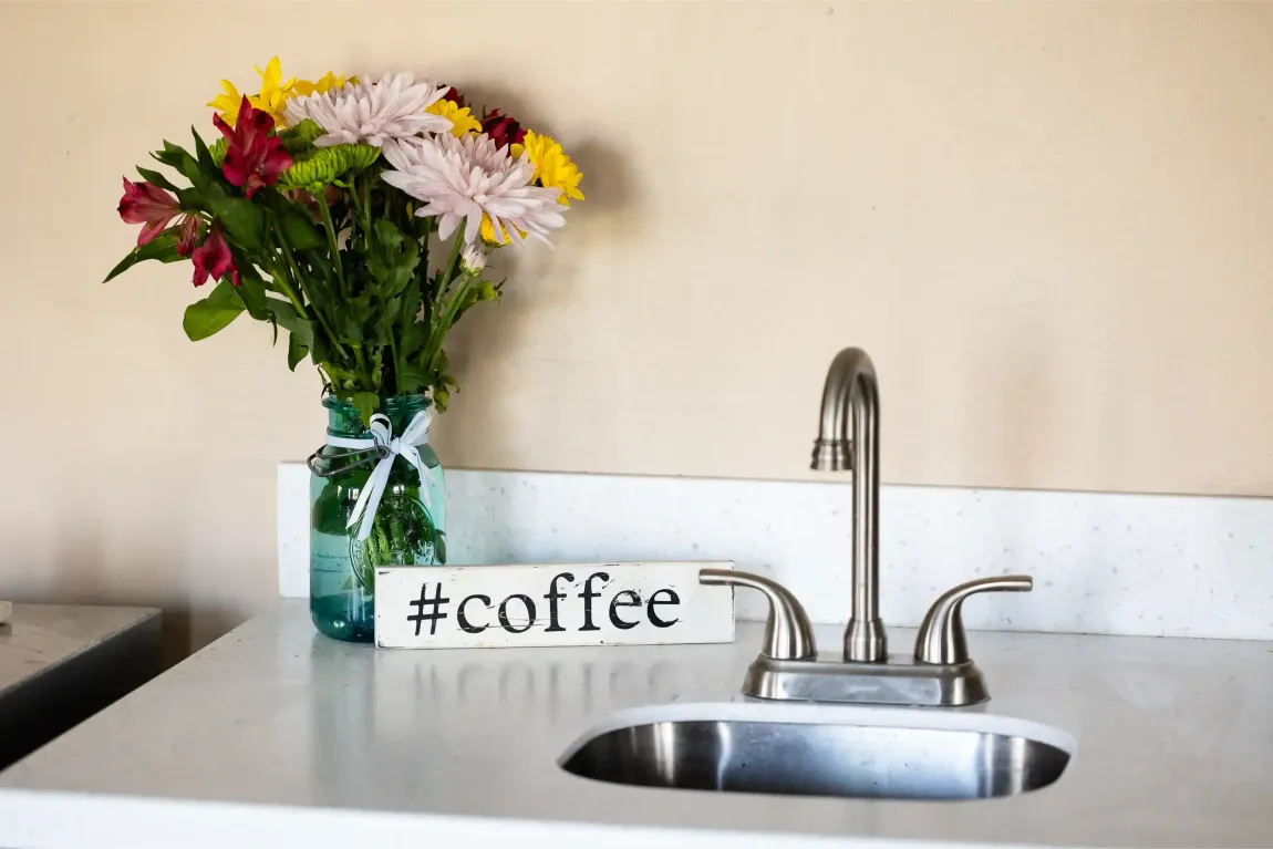 A kitchen sink with a vase of flowers and a sign that says coffee